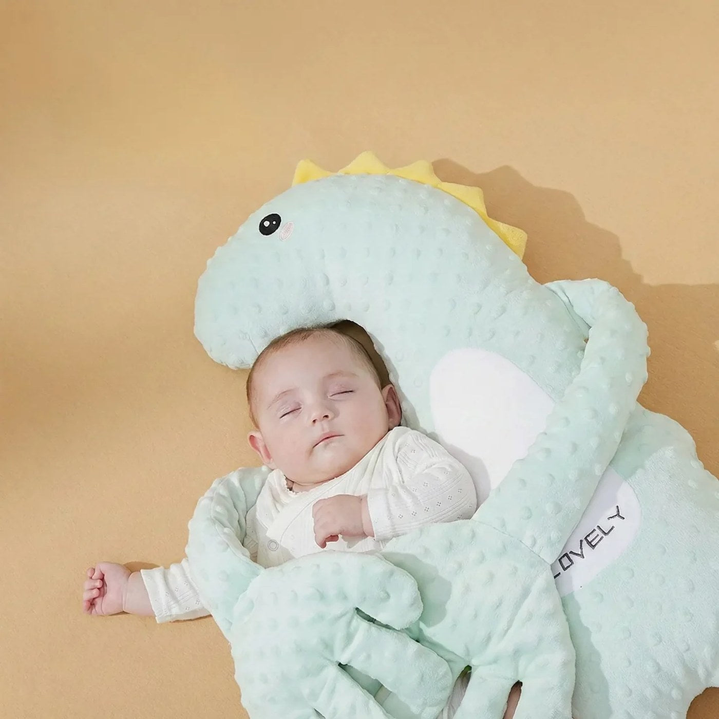 Un bébé installé contre le doudou dino, les bras repliés sur lui